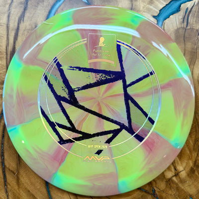 A disc golf disc with a vibrant iridescent finish showing shades of lime green, pink, and yellow, featuring a black geometric pattern and gold foil stamping on a wooden surface.
