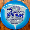 A blue and white Innova Mamba disc golf disc with a blue foil stamp of a coiled snake and the model name 'Mamba' on a wooden surface.