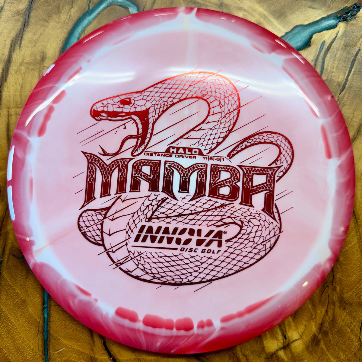 A pink and white disc golf driver featuring a red snake graphic and the text 'Mamba' and 'Innova Disc Golf'.