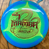 An Innova Mamba disc golf disc featuring a blue and neon green gradient design with a red snake graphic and the word 'MAMBA' in the center, shown on a wooden surface.